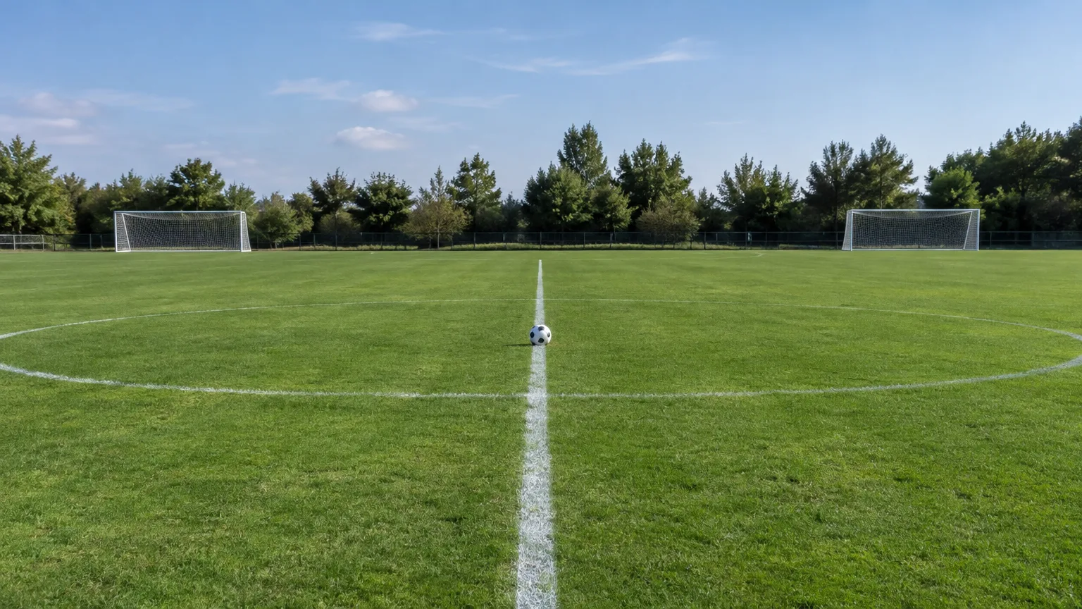Ein Ball liegt auf dem Anstoßpunkt eines leeren Fußballplatzes.